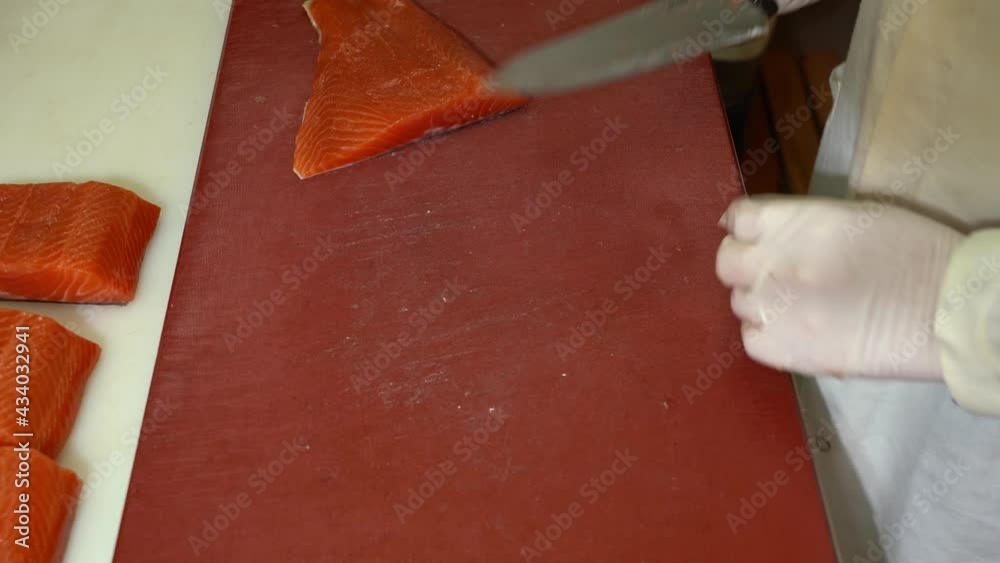 Chef cutting smoked salmon fillets and sliding it off to nearby table - top down view