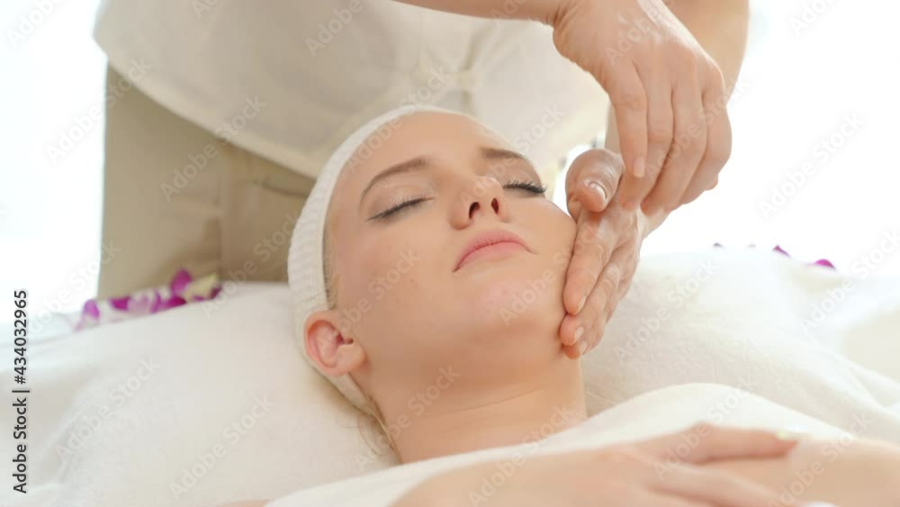 Young beautiful Caucasian woman lying on spa bed get facial massage treatment with aroma essential oil skincare from massage therapist at beauty salon. Wellness health care body massage spa concept. Young beautiful Caucasian woman lying on spa bed get facial massage treatment with aroma essential oil skincare from massage therapist at beauty salon. Wellness health care body massage spa concept.