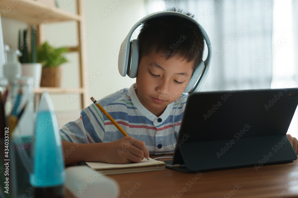 Asian boy learning online via internet with a tutor on a tablet digital with headphone Asian boy learning online via internet with a tutor on a tablet digital with headphone