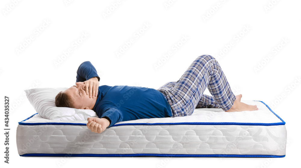 Young man lying on soft mattress against white background