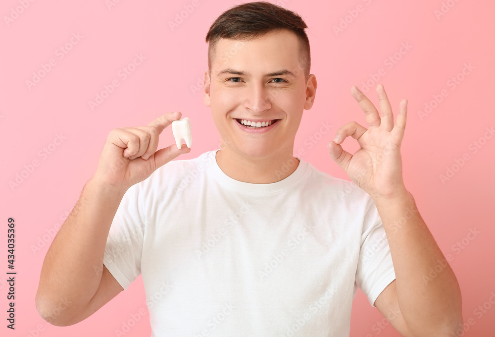 Young man with plastic tooth showing OK on background Young man with plastic tooth showing OK on background