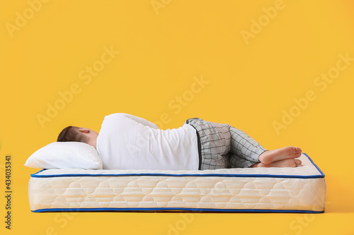 Young man lying on soft mattress against color background