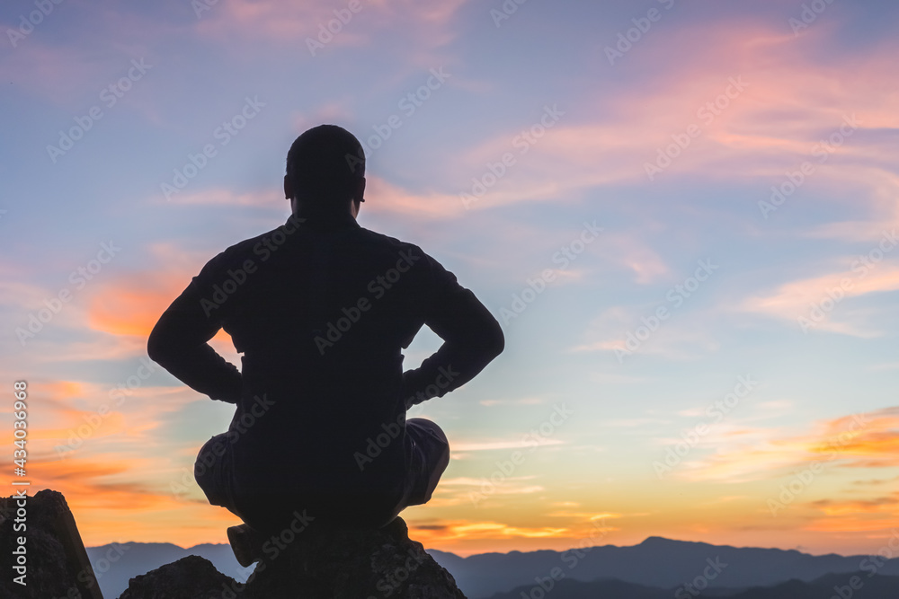 Silhouette male practicing yoga on mountain sunset background