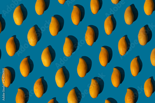 Trendy sunlight summer pattern made with yellow mango on bright light blue background. Minimal summer concept.