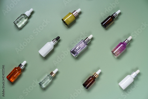 Different glass bottles with serum or oil on green background. Trending shadow. Cosmetic mockup. Top view with copy space. Flat lay.
