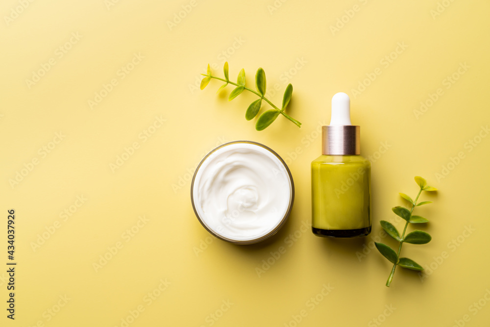 Set of natural cosmetics for face care serum bottle and cream on yellow background, top view