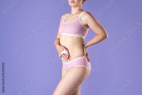 Woman massaging belly with massage brush on purple background