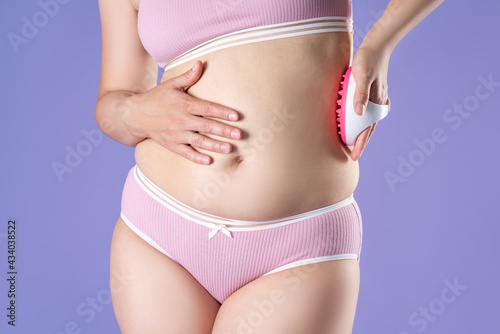 Woman massaging belly with massage brush on purple background