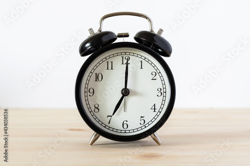 Classic black alarm clock on wooden table with white background and copy space