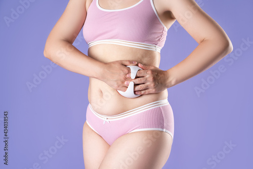 Woman massaging belly with massage brush on purple background