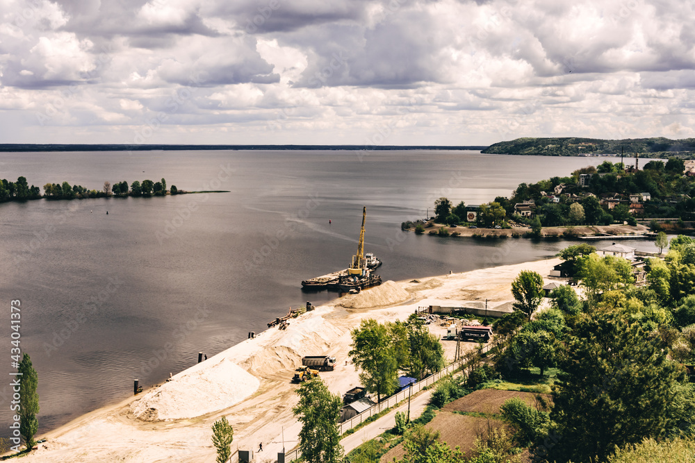 excavator washes the sand by the river under the sky with clouds