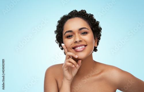 beauty and people concept - portrait of happy smiling young african american woman with moisturizer on her finger tip over blue background