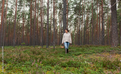 picking season and leisure people concept - young woman with mushrooms in wicker basket walking in forest © Syda Productions