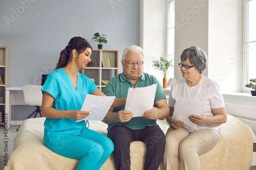 Professional home care nurse helps senior patients fill informed exam consent, sign homecare agreement, understand test result or health insurance details. Grandparents discuss caretaker service costs