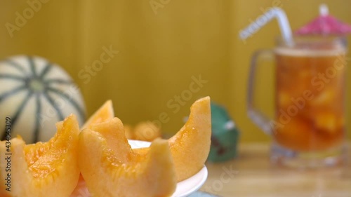 Sliced yellow juicy Kharbuja kept on a ceramic plate rotating on a turntable - Summer fruit India. Closeup shot of a tropical fruit drink inserted with a straw and a whole fruit placed together on ... photo