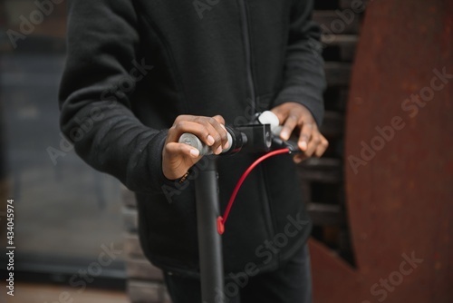 Closeup of african american man holding handle of a black stand-up scooter, blurred background