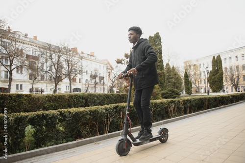 afro american guy rides an electric scooter against the background of a wall, a student uses eco transport