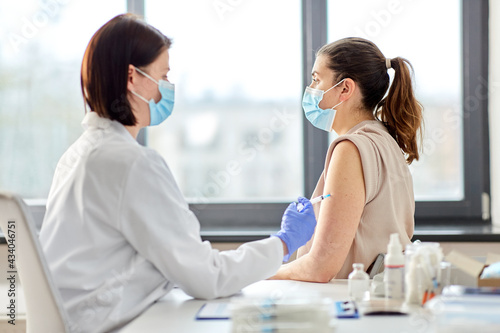 health  medicine and pandemic concept - female doctor or nurse wearing protective medical mask with syringe vaccinating patient at hospital