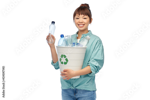 recycling, waste sorting and sustainability concept - smiling young asian woman holding rubbish bin with plastic bottles over white background