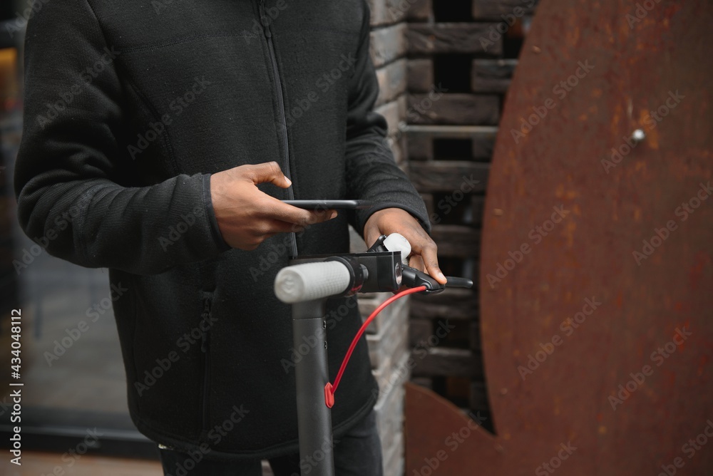 Closeup of african american man holding handle of a black stand-up scooter, blurred background