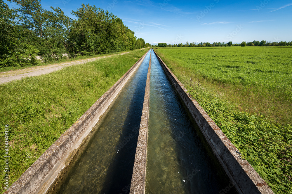 Two small concrete irrigation canals in the countryside, Padan Plain or Po valley (Pianura Padana, Italian). Mantua province, Italy, southern Europe. Two small concrete irrigation canals in the countryside, Padan Plain or Po valley (Pianura Padana, Italian). Mantua province, Italy, southern Europe.