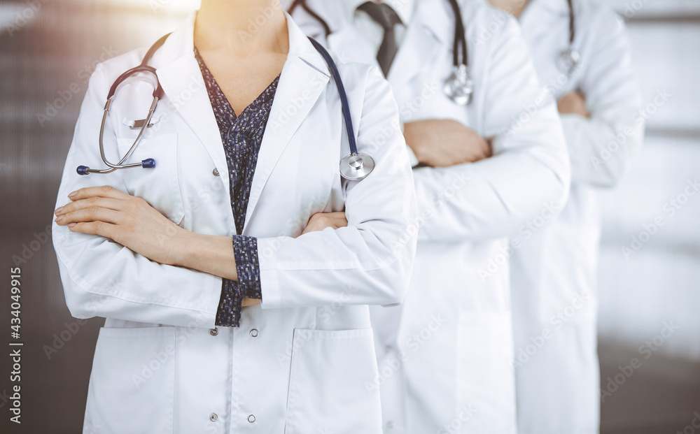 Doctors standing as a team with arms crossed in sunny clinic. Medical help, insurance and medicine concept Doctors standing as a team with arms crossed in sunny clinic. Medical help, insurance and medicine concept
