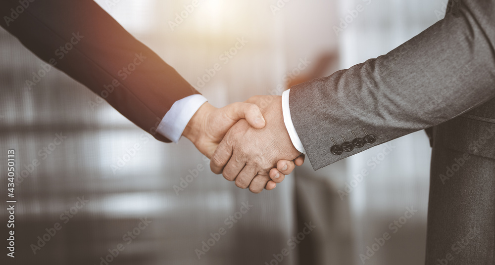 Business people standing and shaking hands in sunny office, close-up. Handshake and marketing