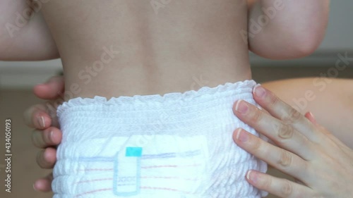 Mothers hands put soft diaper on baby. Toddler diaper. Diapers panties. Dry pants for active children. Baby care.