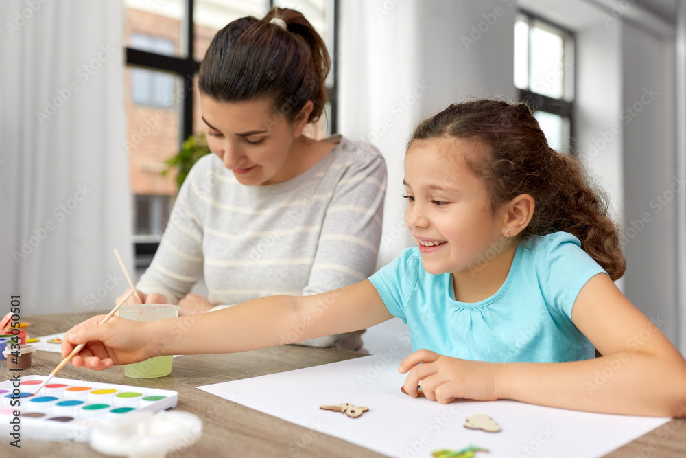 family, motherhood and leisure concept - happy smiling mother spending time with her little daughter drawing or painting wooden chipboard items with colors at home family, motherhood and leisure concept - happy smiling mother spending time with her little daughter drawing or painting wooden chipboard items with colors at home