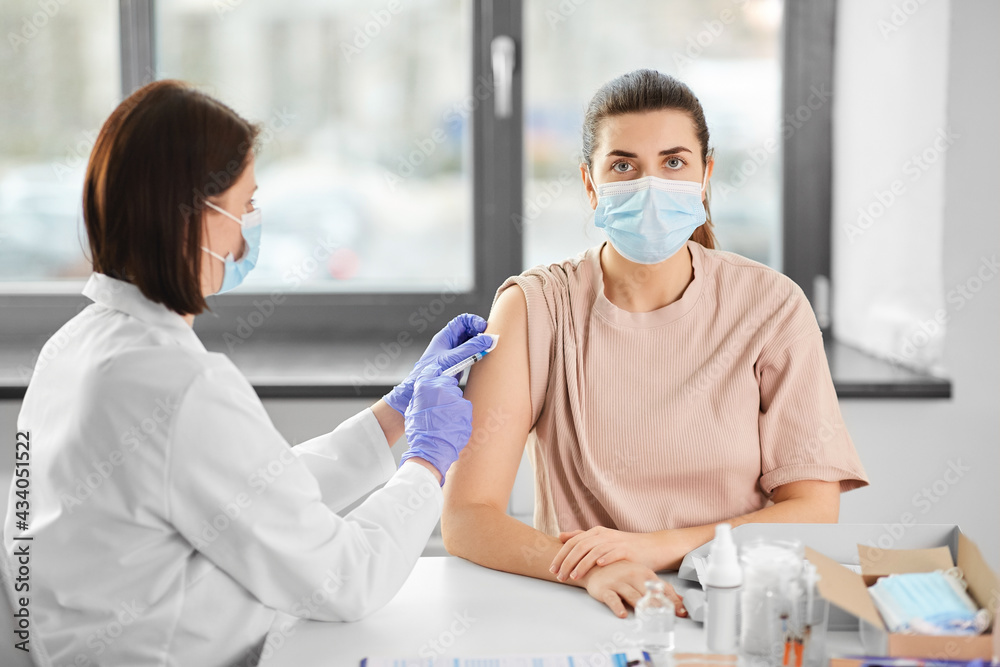 health, medicine and pandemic concept - female doctor or nurse wearing protective medical mask with syringe vaccinating patient at hospital health, medicine and pandemic concept - female doctor or nurse wearing protective medical mask with syringe vaccinating patient at hospital