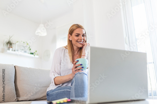 Positive young woman freelancer watching video in blog on netbook and having a coffee at comfortable home. Beautiful young business woman working on laptop.Freelancer connecting to internet