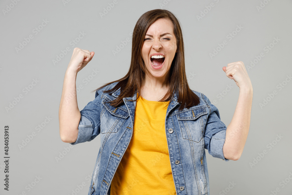 Young happy caucasian woman 20s wearing casual denim jacket yellow t-shirt do winner gesture clench fist celebating scream isolated on grey color background studio portrait. People lifestyle concept Young happy caucasian woman 20s wearing casual denim jacket yellow t-shirt do winner gesture clench fist celebating scream isolated on grey color background studio portrait. People lifestyle concept