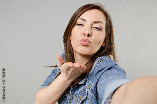 Close up young girlfriend lovely happy caucasian woman 20s wear casual denim jacket yellow t-shirt doing selfie shot on mobile phone blowing air kiss isolated on grey color background studio portrait