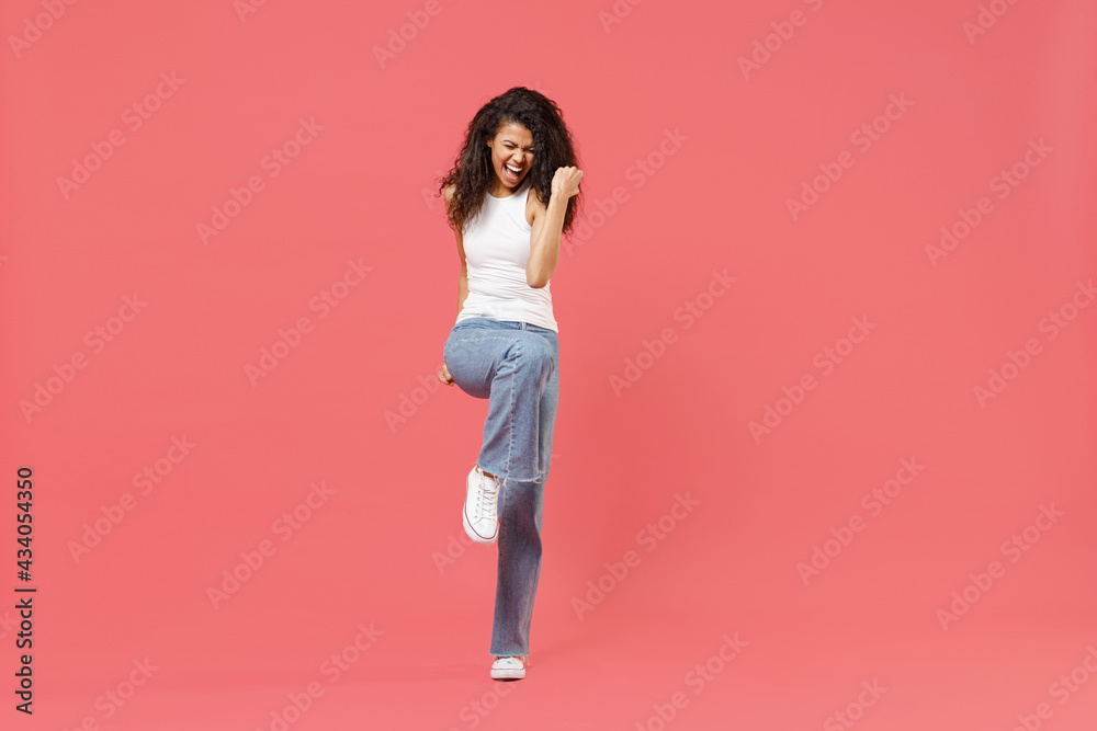 Full length young fun overjoyed happy friendly positive african american woman 20s in casual white tank shirt do winner gesture clench fist isolated on pink color background. People lifestyle concept Full length young fun overjoyed happy friendly positive african american woman 20s in casual white tank shirt do winner gesture clench fist isolated on pink color background. People lifestyle concept