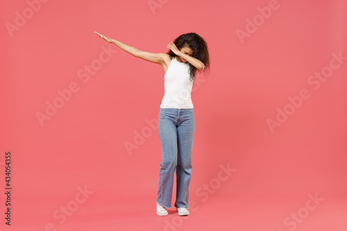 Full length young african american woman 20s wear casual white tank shirt doing dab hip hop dance hands move gesture youth sign hiding covering face isolated on pink color background studio portrait. photo