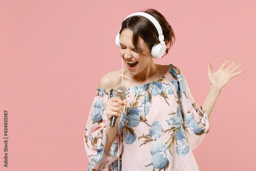 Young singer woman with short hairdo wearing trendy stylish blouse headphones listen to music dancing sing song in microphone in karaoke club spread hands isolated on pastel pink background studio Young singer woman with short hairdo wearing trendy stylish blouse headphones listen to music dancing sing song in microphone in karaoke club spread hands isolated on pastel pink background studio