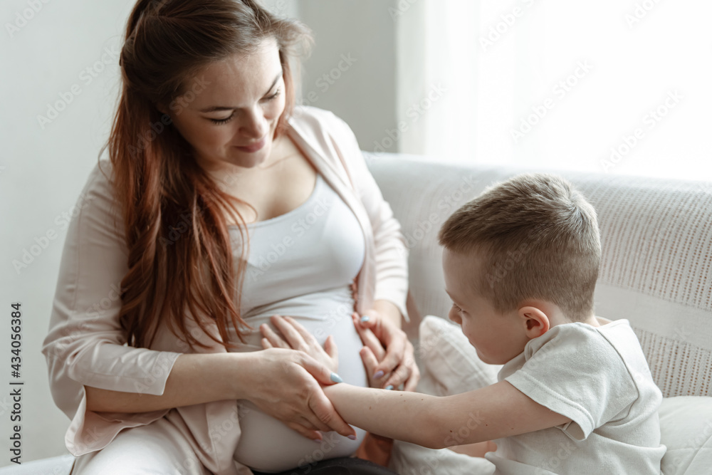 A young pregnant woman is sitting on the couch with her little son. A young pregnant woman is sitting on the couch with her little son.