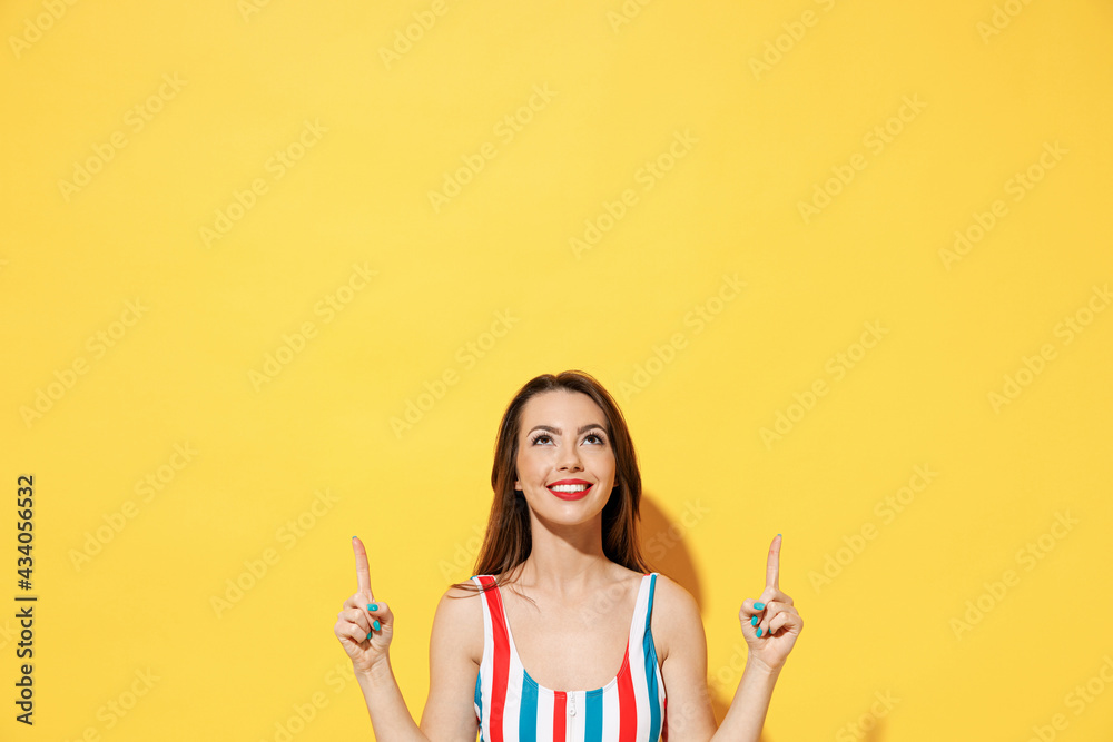Happy young woman wear red blue swimsuit pointing fingers hands above on copy space mock up promo area isolated on vivid yellow color wall background studio Summer hotel pool sea rest sun tan concept Happy young woman wear red blue swimsuit pointing fingers hands above on copy space mock up promo area isolated on vivid yellow color wall background studio Summer hotel pool sea rest sun tan concept