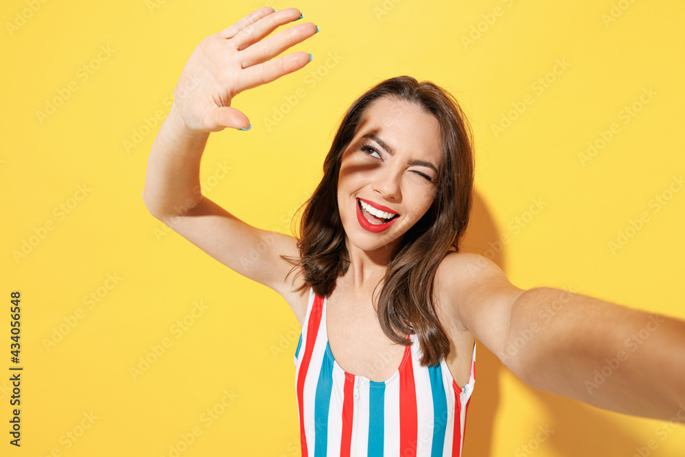 Close up happy fun young sexy woman slim body wear striped red blue one-piece swimsuit doing selfie shot isolated on vivid yellow color background studio. Summer hotel pool sea rest sun tan concept. Close up happy fun young sexy woman slim body wear striped red blue one-piece swimsuit doing selfie shot isolated on vivid yellow color background studio. Summer hotel pool sea rest sun tan concept.