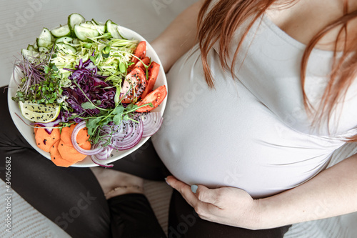 A pregnant woman is holding a large plate of fresh vegetable salad.