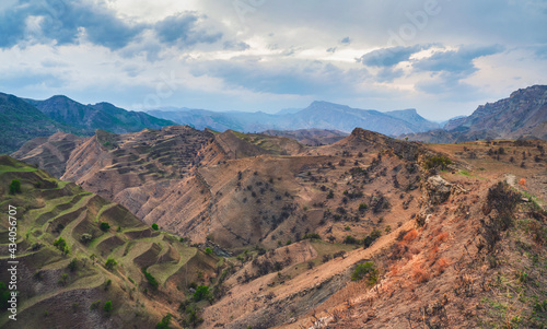 Mountain terraces. A rocky ledge stretching into the distance against the background of red textured mountains covered with sparse vegetation. Panoramic view.