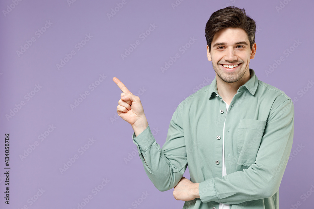 Young fun smiling happy european man 20s in casual mint shirt white t-shirt point index finger aside on workspace area mock up isolated on purple background studio portrait. People lifestyle concept Young fun smiling happy european man 20s in casual mint shirt white t-shirt point index finger aside on workspace area mock up isolated on purple background studio portrait. People lifestyle concept