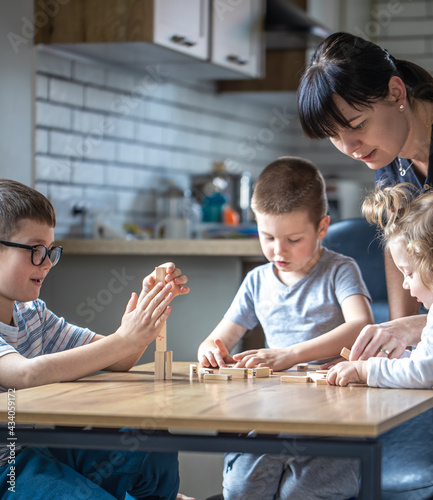 Children with their mother play board at home in the kitchen.