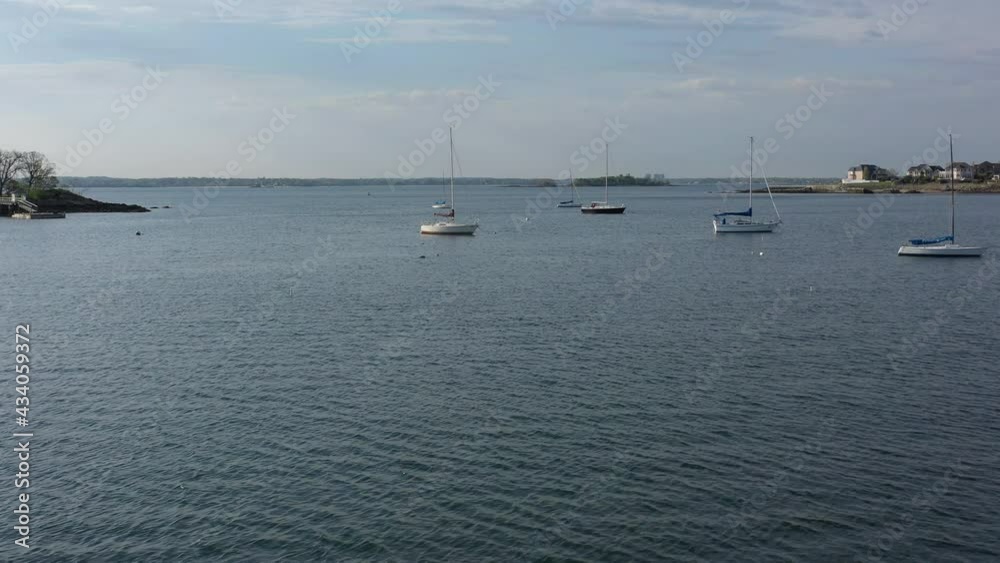 A low altitude drone shot over calm with a few sailboats in the water. The camera dolly in towards the boats and the horizon on a beautiful day with blue skies.
