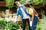 Young man in medical mask asking gardening center worker to help him with choosing plants and flowers