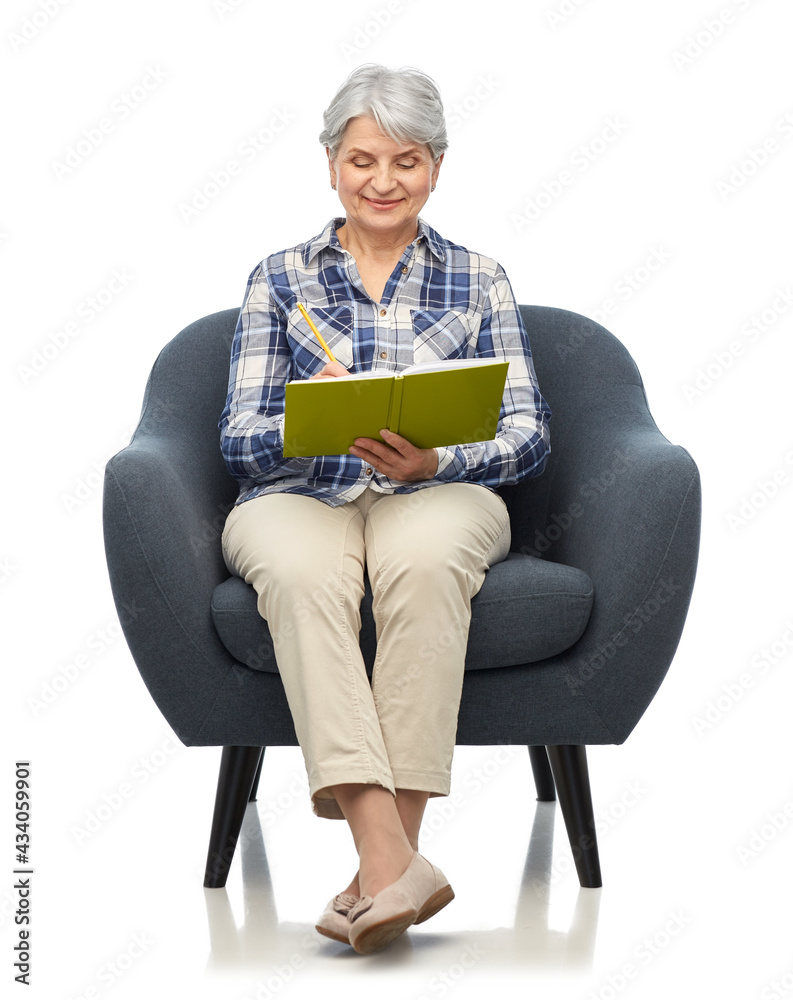 comfort, furniture and old people concept - smiling senior woman sitting in modern armchair and writing to diary over white background comfort, furniture and old people concept - smiling senior woman sitting in modern armchair and writing to diary over white background