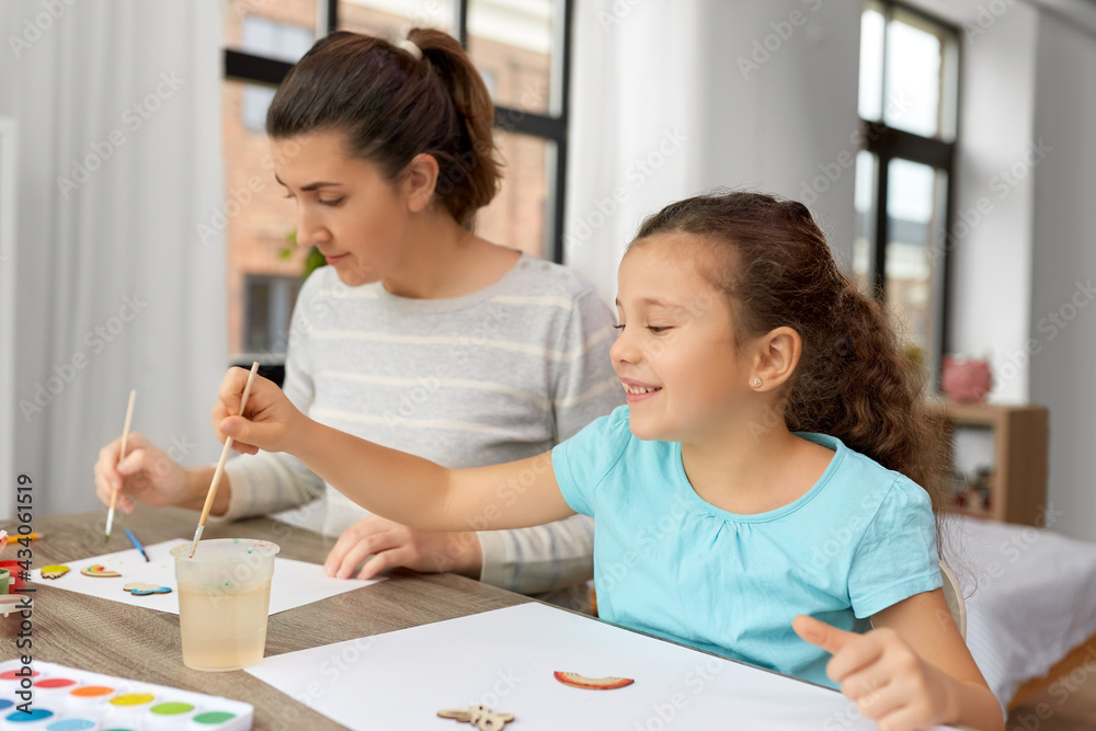 family, motherhood and leisure concept - happy smiling mother spending time with her little daughter drawing or painting wooden chipboard items with colors at home