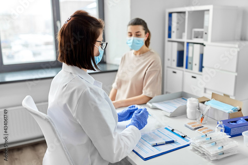 health, medicine and pandemic concept - female doctor or nurse wearing protective medical mask and gloves opening package with syringe for vaccination and patient at hospital