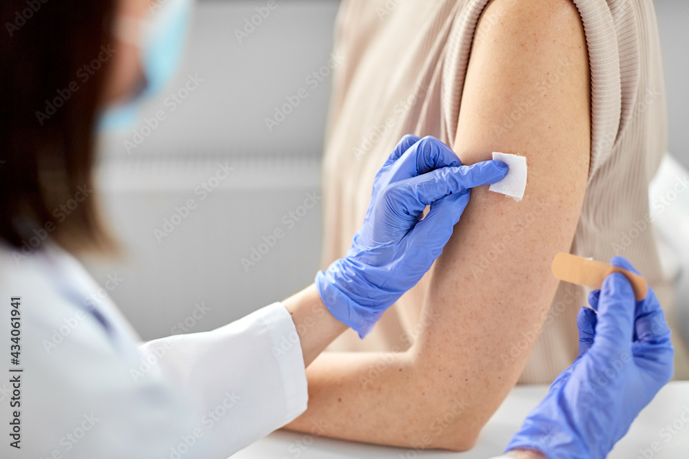 health, medicine and vaccination concept - close up of doctor wearing protective medical mask and gloves attaching adhesive medical plaster or patch to patient at hospital health, medicine and vaccination concept - close up of doctor wearing protective medical mask and gloves attaching adhesive medical plaster or patch to patient at hospital