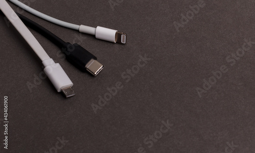 USB charging cables for smartphones and tablets in white and black on a dark background. An irreplaceable thing for modern electronics.